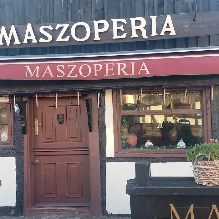 Drewniane drzwi wejściowe dzielone na dwie połówki, pod czerwoną markizą z napisem Maszoperia