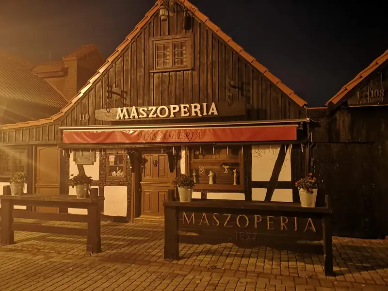 Dom Maszoperii o zmierzchu, z podświetlonym szyldem i markizą
